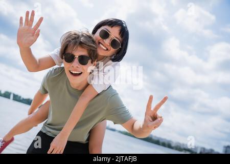 cheerful interracial couple showing victory signs while having fun near river Stock Photo