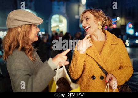 Two forty women talking and laughing carefree outdoors at Christmas market in the city center holding shopping bags - people lifestyle and holiday con Stock Photo