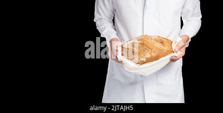Close-up of a baker in white uniform holding a wholemeal loaf in his hands isolated on black background Stock Photo