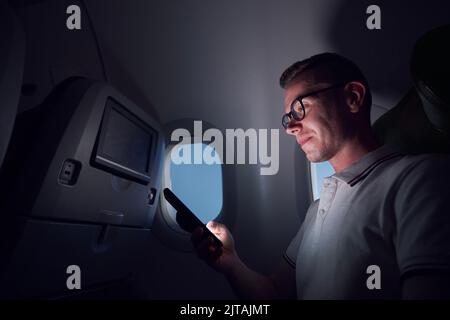 Man traveling by airplane. Passenger using phone during night flight. Stock Photo