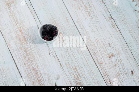 Black blackberries in bowl on wooden background. copy space, top view. Harvest Concept Stock Photo