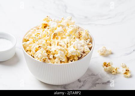 Classic salted popcorn in a white bowl, white marble background, copy space. Stock Photo