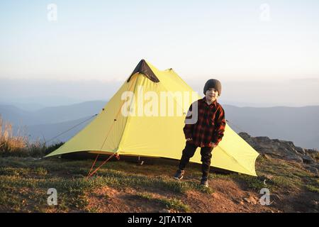 Small kid near yellow tent in autumn mountains. Travel with child concept Stock Photo