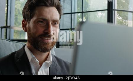 Happy dreaming smiling Caucasian bearded adult 40s man work with computer online write article looking away dreaming thinking pondering business Stock Photo