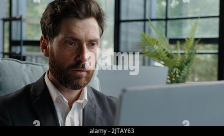 Close up caucasian bearded middle aged 40s freelancer man worker user manager company CEO employee businessman working on computer concentrated Stock Photo