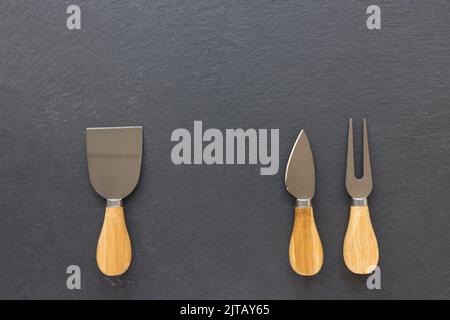 Set of cheese knives with wooden handles. Fork and spatula on black background. Shabby appearance. Top view, copy space Stock Photo