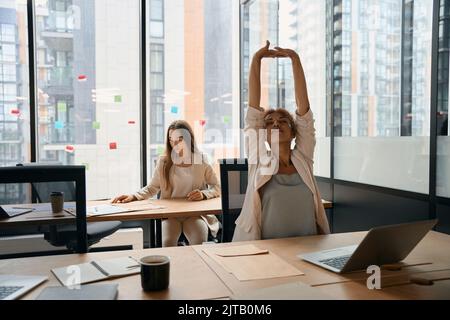 Smiling woman stretching arms up sitting in bright office Stock Photo