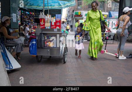 A street scene under the El in Corona Queens featuring a crying child, a mother the kid's scooter and vendors. New York City, 2022. Stock Photo