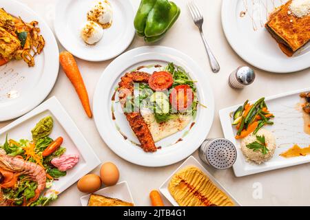 Greek cuisine recipes with grilled octopus, chickpea hummus, shrimp salad, arron with vegetables, moussaka and boiled eggs Stock Photo