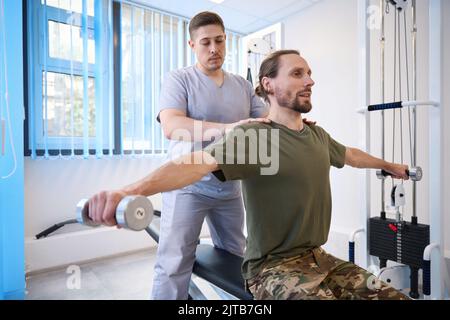Patient doing special exercises with dumbbells under supervision of instructor Stock Photo