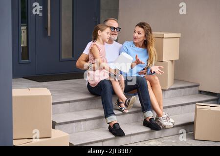 Cheerful family are sitting on steps near house Stock Photo