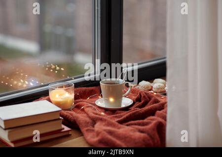 cup of tea, books and candle burning on windowsill Stock Photo