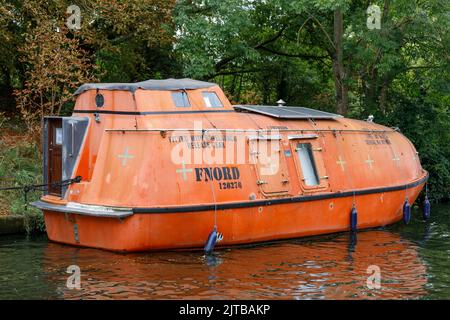 A closed liferaft moored on a riverbank on the River Thames and used as a home or houseboat. Stock Photo