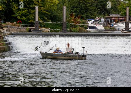 Two men in a small boat fishing below a weir on the River Thames in summer Stock Photo