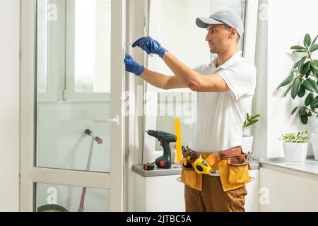 a repairman repairs, adjusts or installs metal-plastic windows in the apartment. glazing of balconies, loggias, verandas in house. production of Stock Photo