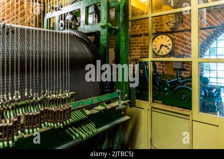 The clockwork of St. Lebuïnus Church in Deventer, one of nine historic Hanseatic towns on the IJssel river, province of Overijssel, Netherlands, was made in 1862 by the Parisian clockmaker Amédée-Philippe Borrel; the playing drum for the carillon was delivered in 1866 by the Deventer iron foundry Nering Bögel. The green-painted mechanism, with its countless pull wires, almost completely fills the cramped chamber inside the tower, with a tower clock visible against the brick wall in the background. Stock Photo