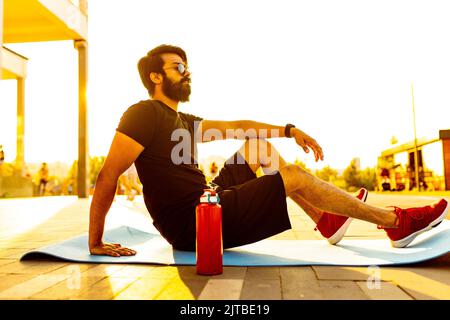 bearded man in black cotton t-shirt warming up outdoor in summer park at sunset gold light Stock Photo