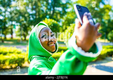 latin hispanic arab woman in green muslim dress with modern bright make up and nose piercing taking selfie at phone camera outdoors Stock Photo