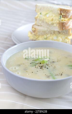 Cream of Celery Soup in a White Bowl with Blurred Egg Salad Sandwich in Background Vertical Stock Photo