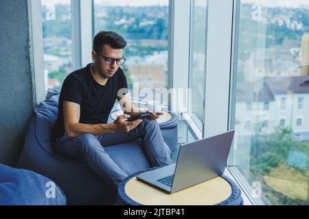 A young businessman is looking for something and typing on a smartphone and drinking fresh black coffee. The concept of a modern successful person. Yo Stock Photo