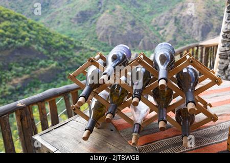 Wooden wine rack with with empty bottles, on a table, with forest and mountains in the background Stock Photo