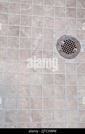 A neutral light beige square tile shower floor with a silver metal drain Stock Photo