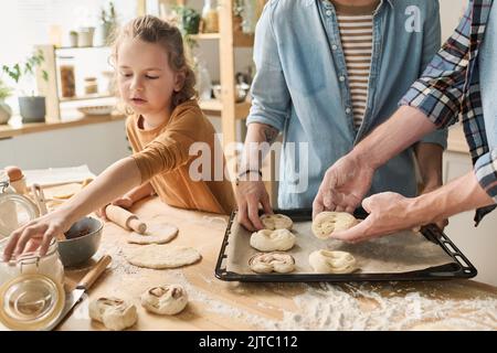 Close-up of family of three putting homemade buns on tray for baking, they cooking together at table Stock Photo