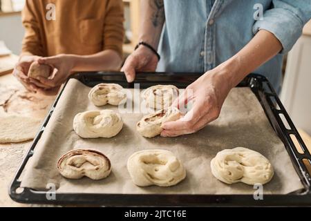 Close-up of mother putting homemade buns on tray for baking with her son helping her Stock Photo