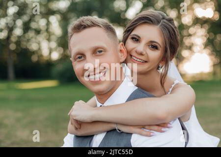 Amused, smiling newlywed married couple of bride in wedding dress and groom hugging gently together, looking at camera Stock Photo