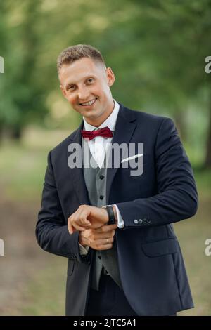 Vertical portrait of confident, handsome smiling blond businessman or groom in formal tuxedo fixing stylish hand watch Stock Photo