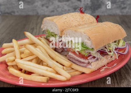 Enormous Italian cold cuts sandwich is loaded with cotto salami, provolone cheese, tomato and onion with a hearty serving of french fries on the side. Stock Photo