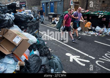 Pedestrians walk between lines of overflowing rubbish bins in East Crosscauseway due to industrial action by Edinburgh council workers. Stock Photo