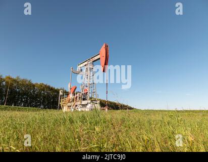 Operating oil and gas well in oil field, profiled against the blue sky. Stock Photo