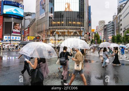 Pedestrians with umbrellas cross the multi-directional scramble crossing intersection known as the Shibuya Crossing in Shibuya Ward, Tokyo, Japan. The intersection is considered the busiest pedestrian intersection in the world. Stock Photo