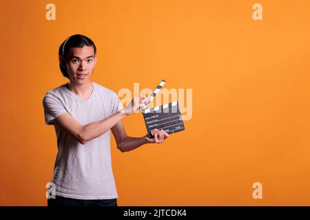 Clapper loader slapping slate, holding film making equipment, movie scene shooting. Cinematography, video production, young smiling asian cameraman assistant looking at camera Stock Photo