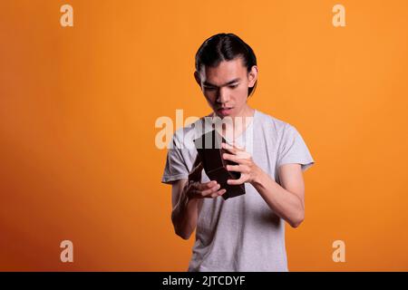 Curious asian man opening gift, looking inside small cardboard box, unboxing present. Young person unpacking surprise, holding delivery parcel with interested facial expression Stock Photo