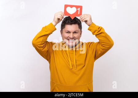 Smiling middle aged man blogger holding likes counter template above head making posts in social networks, wearing urban style hoodie. Indoor studio shot isolated on white background. Stock Photo