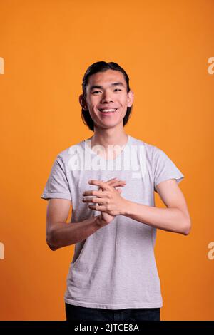 Young cheerful smiling asian man applauding, looking at camera. Positive laughing teenager with joyful facial expression clapping hands, attractive person standing, medium shot portrait Stock Photo