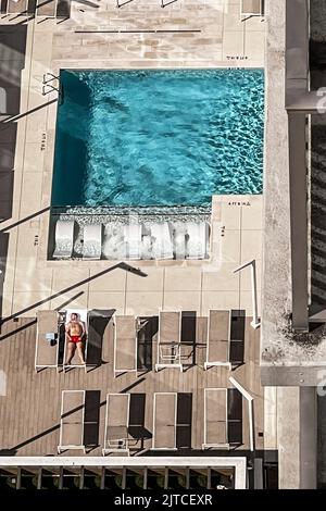 ATLANTA, GA / USA - MARCH 20:  High angle perspective shows lone man laying out by pool on lounge chair on March 20, 2022 in Atlanta, GA. Stock Photo