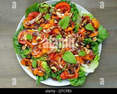 Colorful salad plate with green lettuce, carrot slices, tomatoes, onions, nuts, dried figs, spices and lemon balm leaves top view. Stock Photo