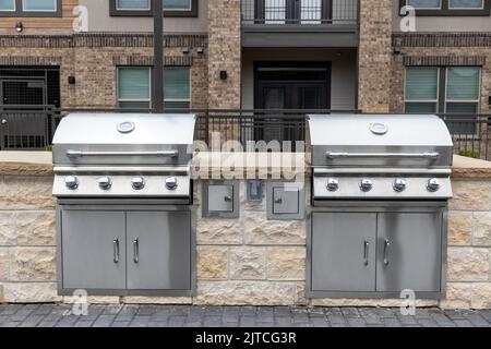 Two outdoor built in barbecue BBQ stainless steel grills at back yard of the residential complex with brick building on background Stock Photo