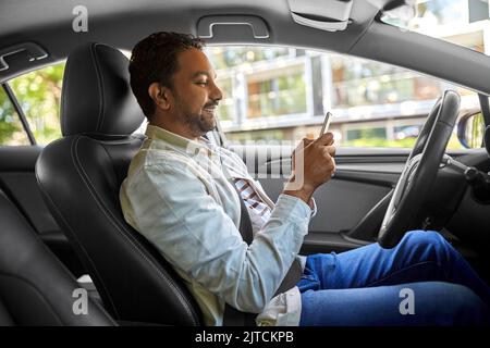 smiling indian man in car using smartphone Stock Photo