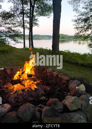 Campfire next to a calm lake in the summer, vertical Stock Photo