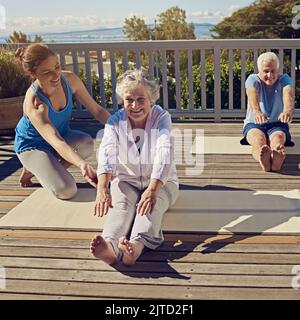 Fit and active in their golden years. a senior couple doing yoga together with an instructor on their patio outside. Stock Photo