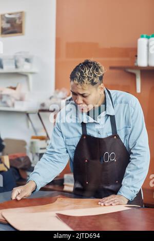 Vertical portrait of young craftsman working with leather in tannery shop and creating handmade pieces Stock Photo