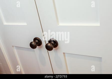 A set of double white wood interior doors with dark black or oil rubbed broze doorknobs for a closet or room door opening Stock Photo