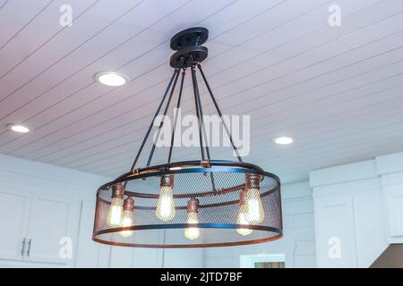 An industrial lighting fixture with Edison bulbs in an updated and remodeled all white modern kitchen Stock Photo