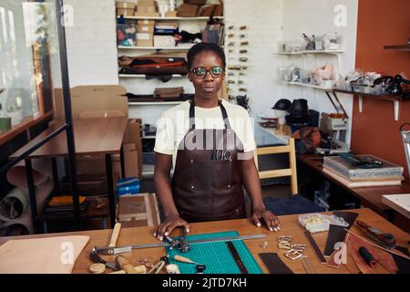 Waist up portrait of young female artisan standing in leatherworking shop and smiling at camera proud with small business Stock Photo