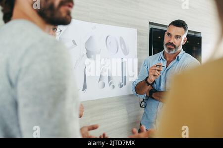 Creative businesspeople having a discussion while working with design drawings in a modern office. Group of innovative designers planning a renewable Stock Photo