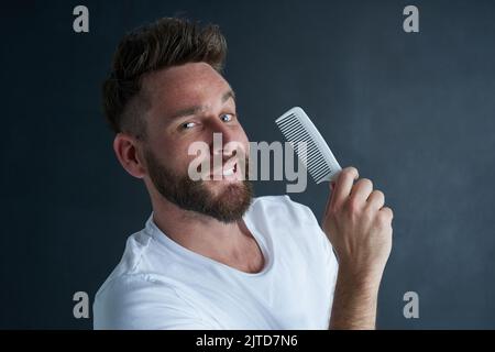 Theres only one tool for the job. Portrait of a handsome young man posing against a dark background with a comb in his hand. Stock Photo